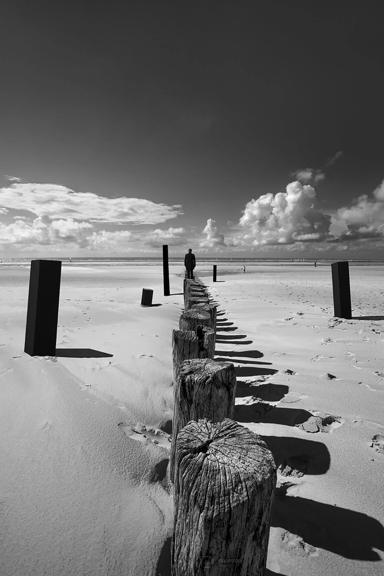 Un homme face à la mer immobile sur des pieux entouré de colonnes noires photo noir et blanc art berck palge boulogne sur mer lille paris marseille