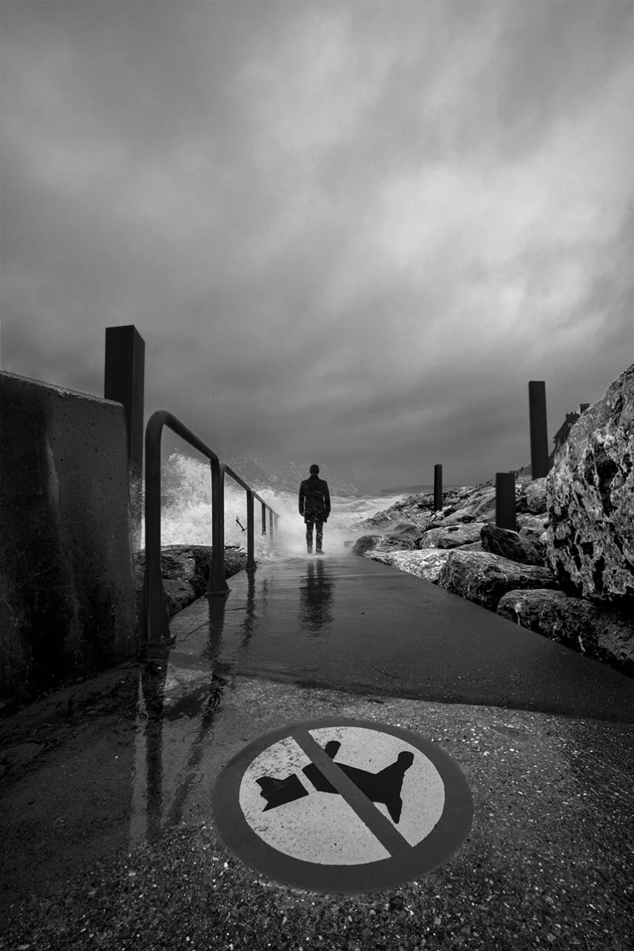 photo art en noir et blanc d'un homme en bas de la digue dans la tempête violent entouré de colonnes noires à wissant florent photographe