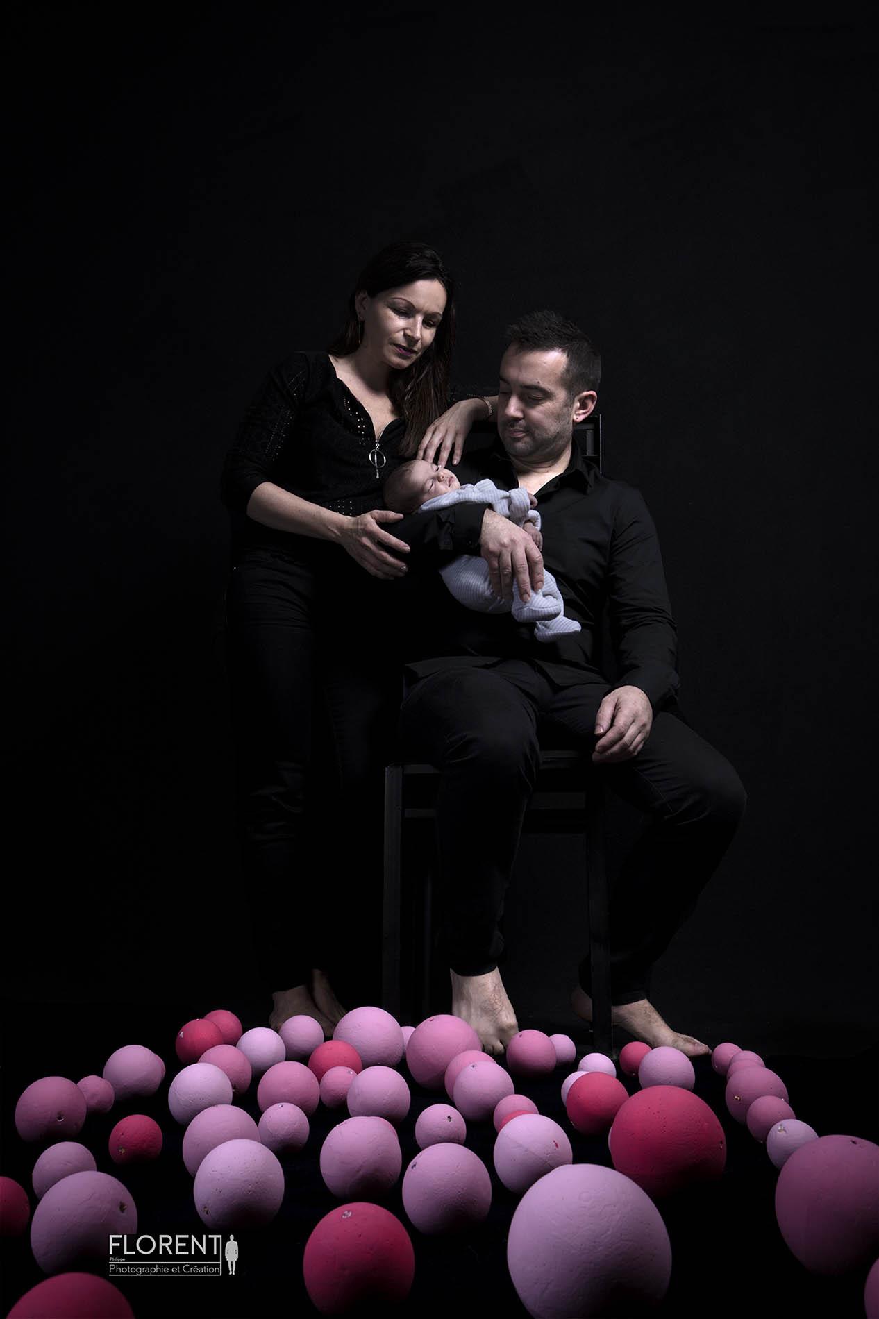 portrait bébé douceur de bébé dans les bras de papa et maman entourés de boules roses sur fond noir florent studio photographe boulogne sur mer lille le touquet paris amiens