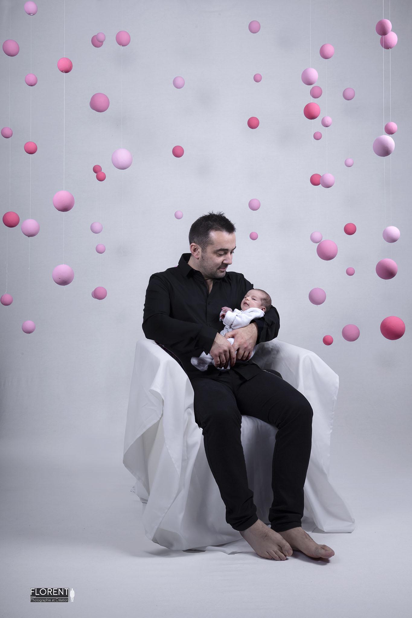 photographe bebe studio de bébé dans les bras de papa entouré de véritables boules roses suspendues florent studio boulogne sur mer lille le touquet paris calais