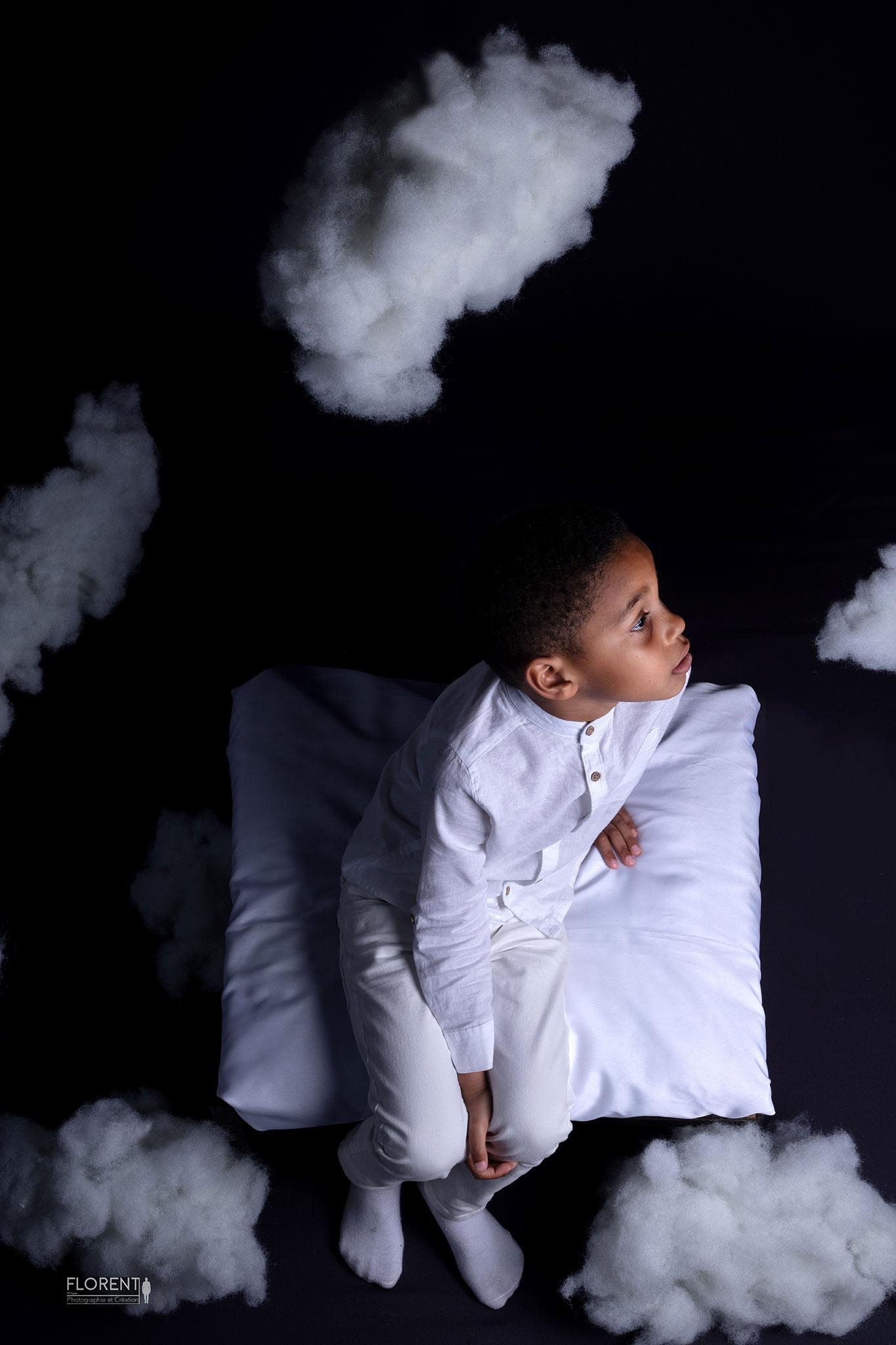photographe enfant vue du dessus d'un enfant en studio photo regardant le décors de nuages magiques